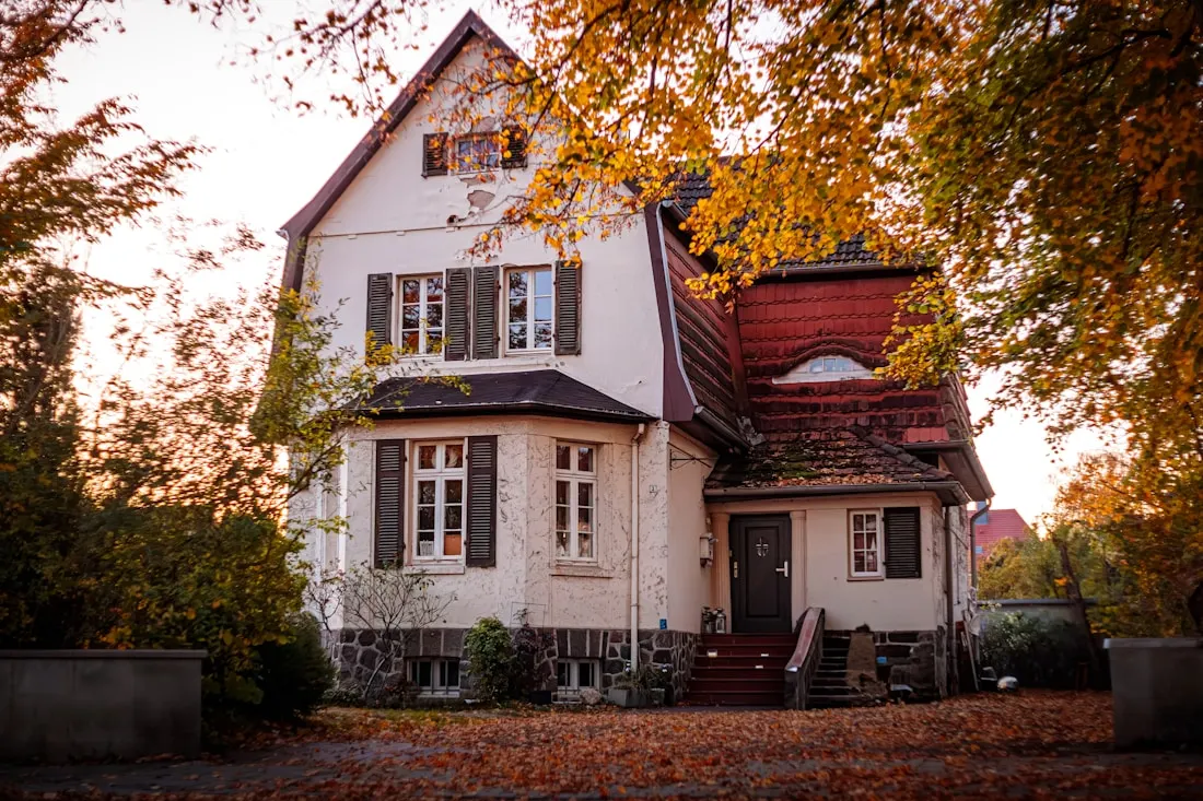 A house under autumn trees, leaves down across the lawn